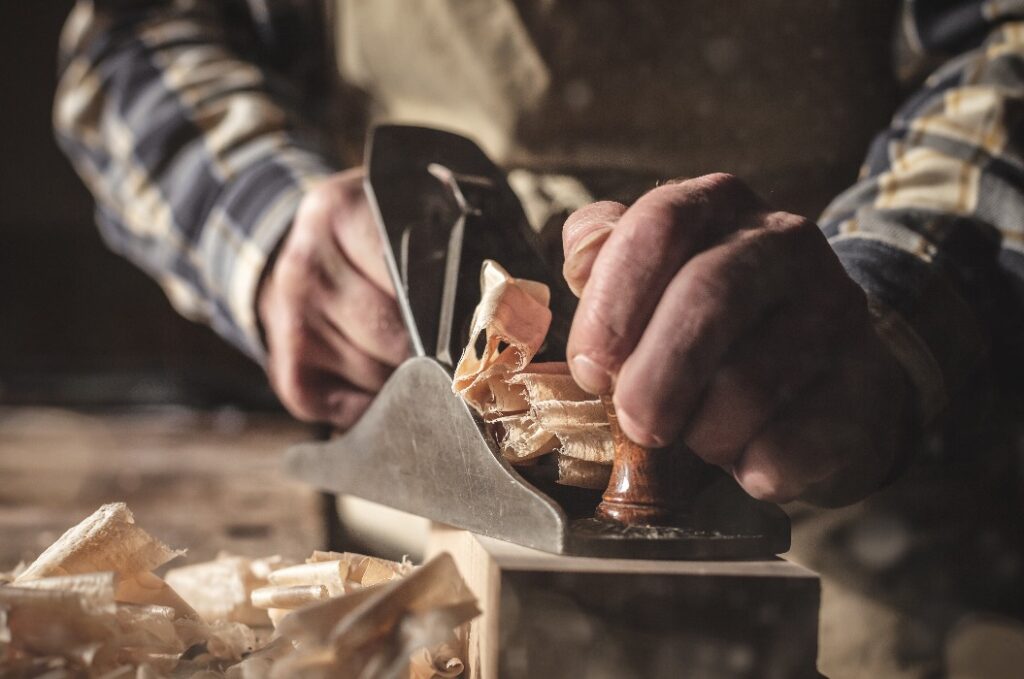 Hände eines Schreiners bei der Arbeit mit dem Hobel