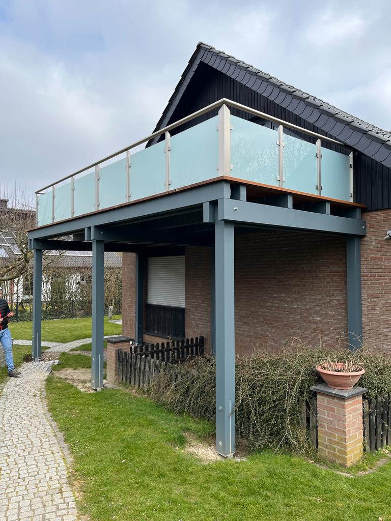 Ein Mann in Jeans steht neben einem modernen Balkon mit Milchglas und grauen Pfeilern