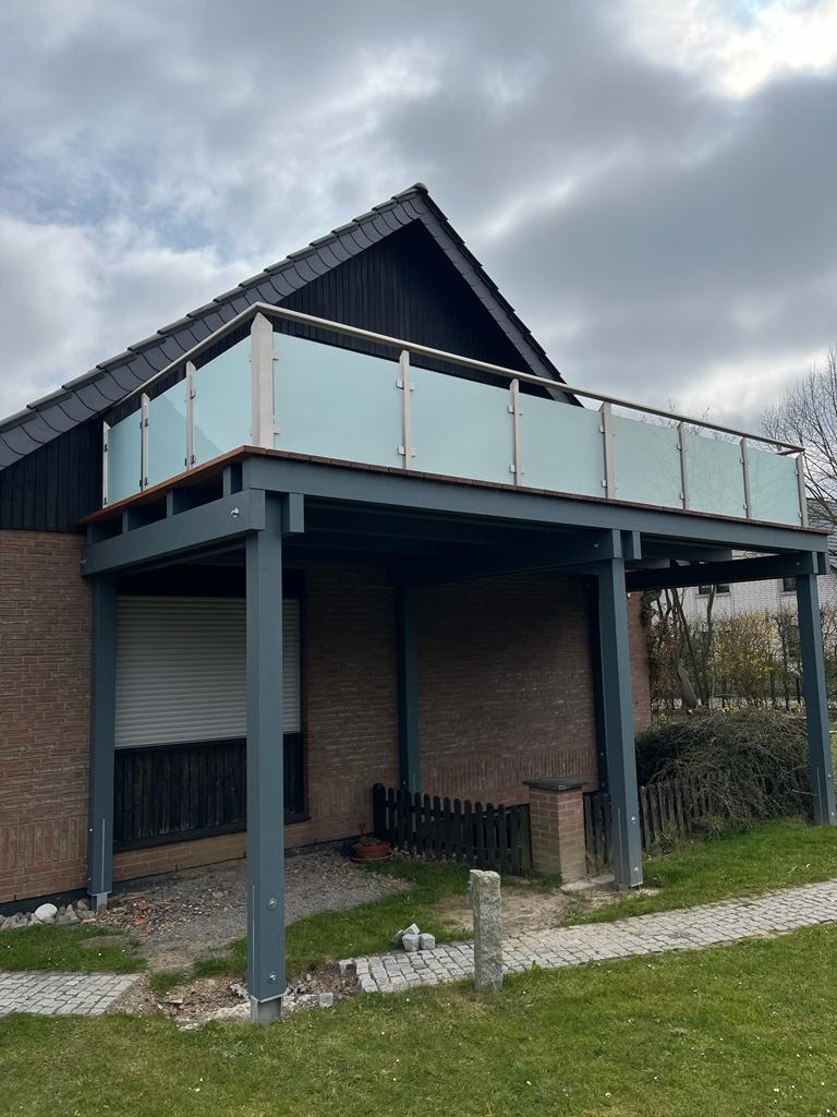 Ein modernes Haus mit einer oberen Terrasse mit Milchglasgeländer und grauen Stahlträgern