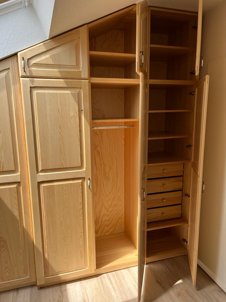 Ein geöffneter, heller Holzkleiderschrank mit Regalen, Schubladen und Hängestange