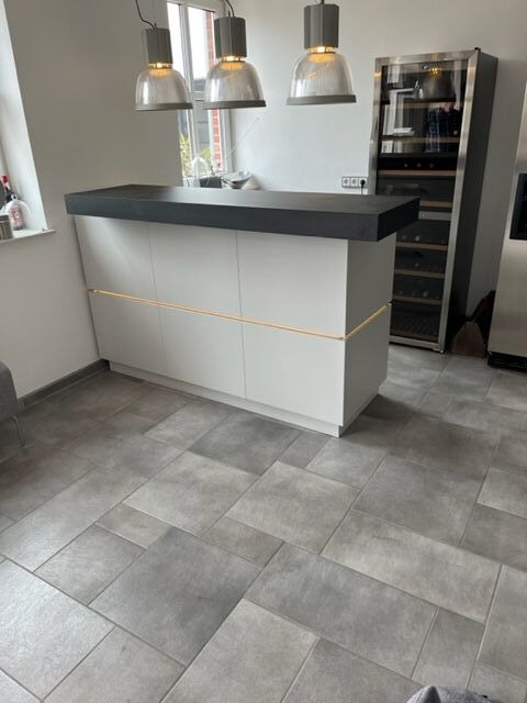 Moderne Küche mit grauen Fliesen, weißer Kochinsel, schwarzen Details und Weinkühlschrank