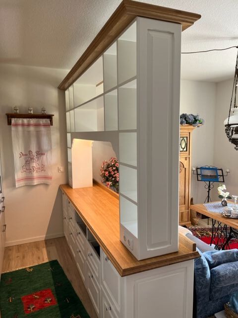 Weißes Regal mit Holzarbeitsplatte trennt zwei Räume, dekorative Blumen im Hintergrund