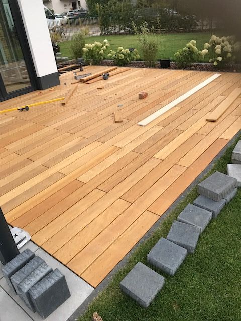 Eine helle Holzterrasse wird gerade gebaut, graue Pflastersteine liegen am Rand