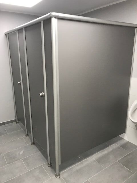 Drei graue Toilettenkabinen mit silbernen Rahmen in einem gefliesten Waschraum