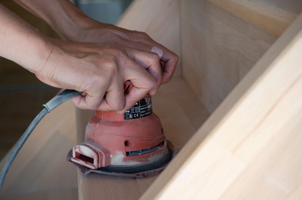 Nahaufnahme einer manuellen Schleifmaschine, die von einer Frau bedient wird, die eine Holztreppe schleift, Do-it-yourself-Konzept